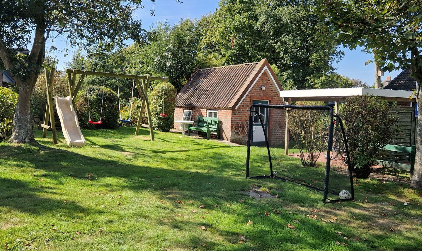 A backyard with a swing set, a brick house, and a covered area.