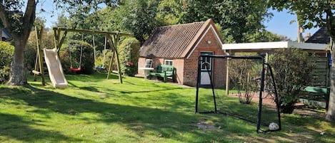 Un patio trasero con un columpio, una casa de ladrillo y un espacio cubierto.