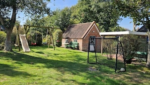 A backyard with a swing set, a brick house, and a covered area. - Babendörpstieg 20, Apt. 1 - 2-room vacation apartment in Nieblum, approx. 55 square meters, ground floor and upper floor (Nieblum)