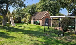 Ein Garten mit Schaukel, einem Ziegelhaus und einem überdachten Bereich.