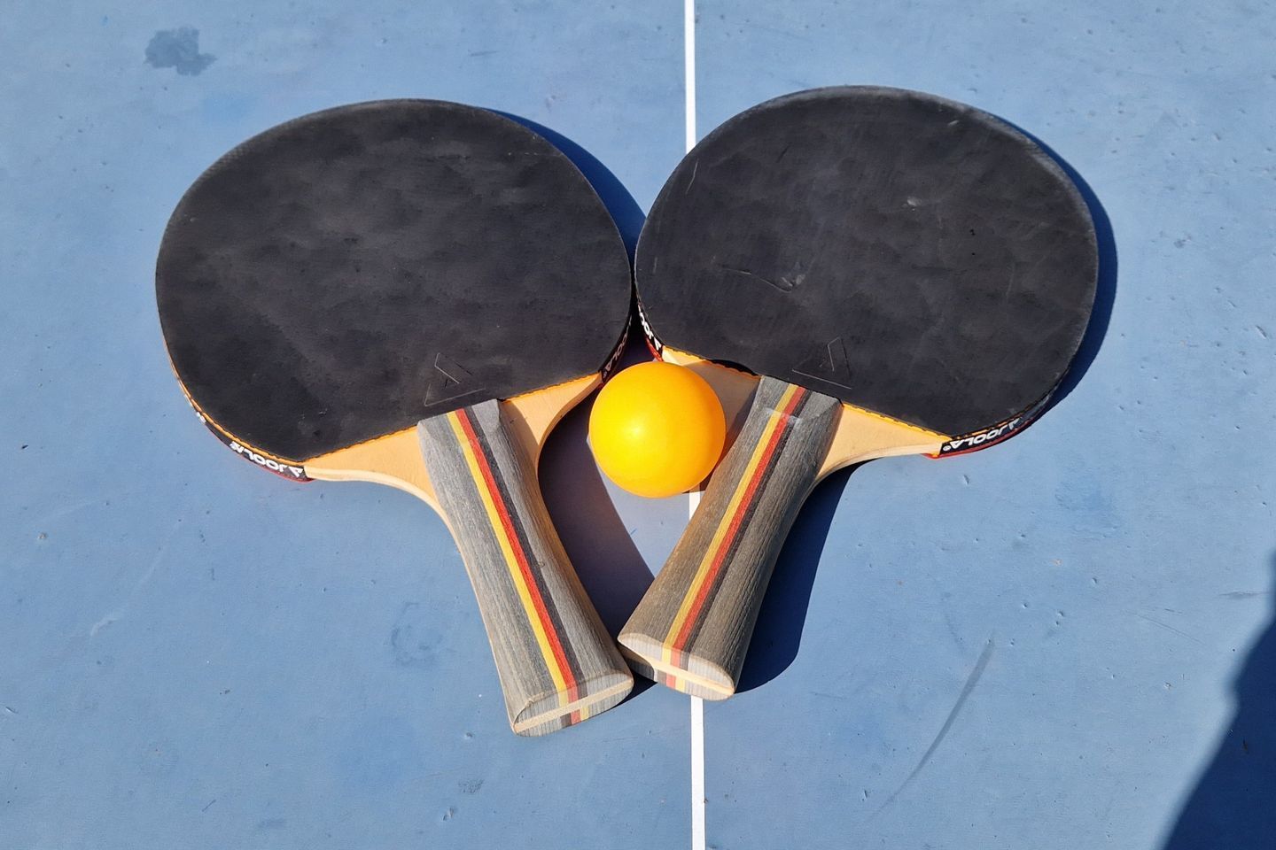 Two ping pong paddles with a yellow ball on a blue surface.