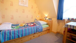 Een enkel bed met een kleurrijk Mickey Mouse dekbed, een nachtkastje met een lamp, en een raam met gordijnen.