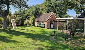 A residential property with a brick house, a swing set, and a covered outdoor area. - Babendörpstieg 20, Apt. 3 - 4-room vacation apartment in Nieblum, approx. 65 square meters, on the 1st floor (Nieblum)