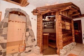 Un sauna rustique en bois, doté d’une entrée en forme d’arche en pierre et d’un sol carrelé en pierre.
