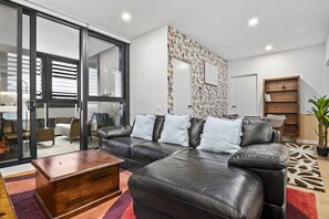 A modern living room with a black leather sofa, a wooden coffee table, and a patterned rug. - High-Rise 2-Bed Apt at Trio Boxhill with Car Park (Box Hill)