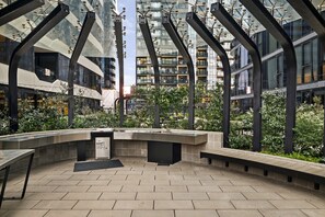 An outdoor seating area with a modern design, featuring a curved bench and a small trash bin. - High-Rise 2-Bed Apt at Trio Boxhill with Car Park (Box Hill)