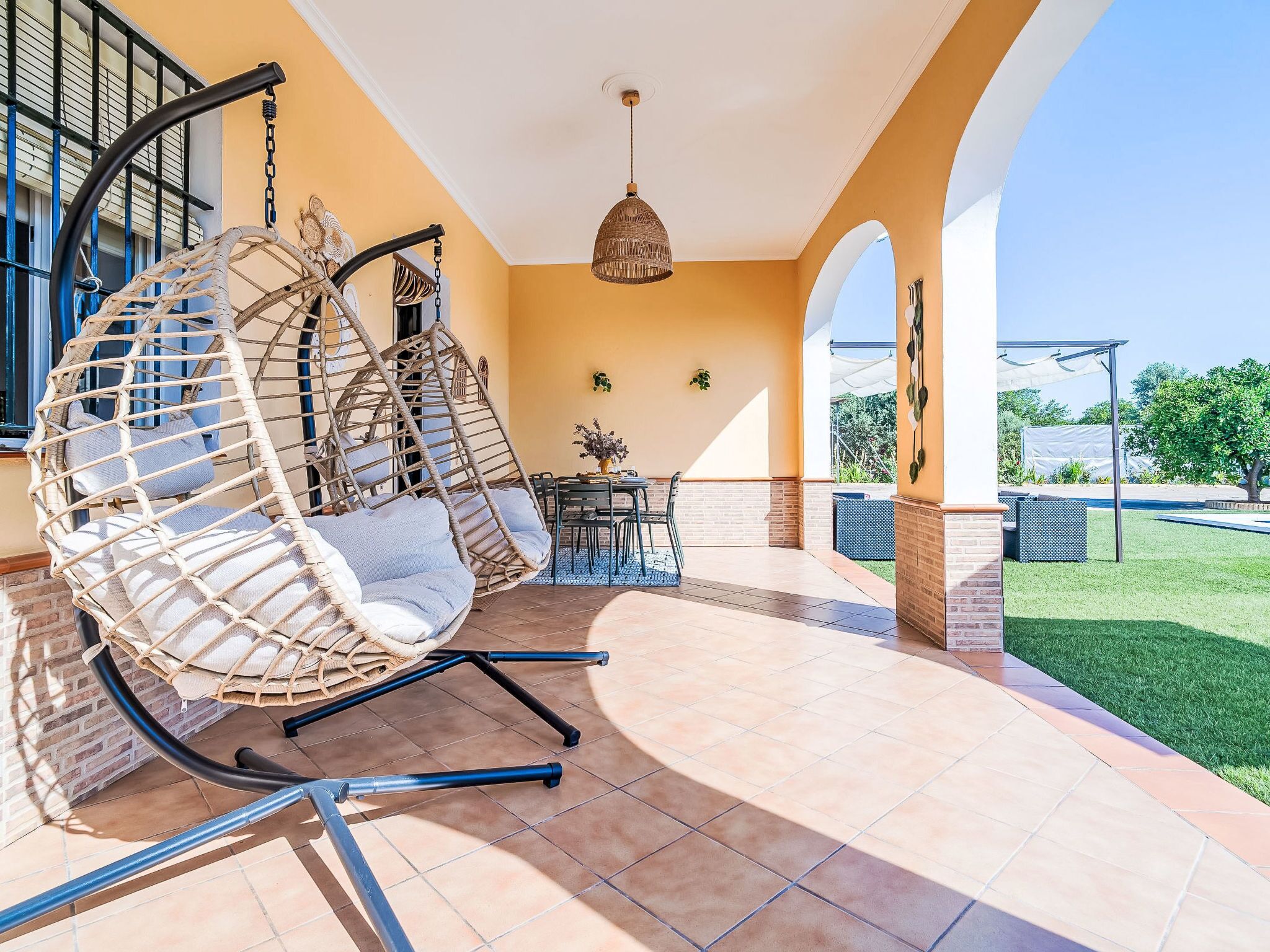 Une terrasse avec un fauteuil suspendu, une table avec des chaises et une vue sur le jardin.
