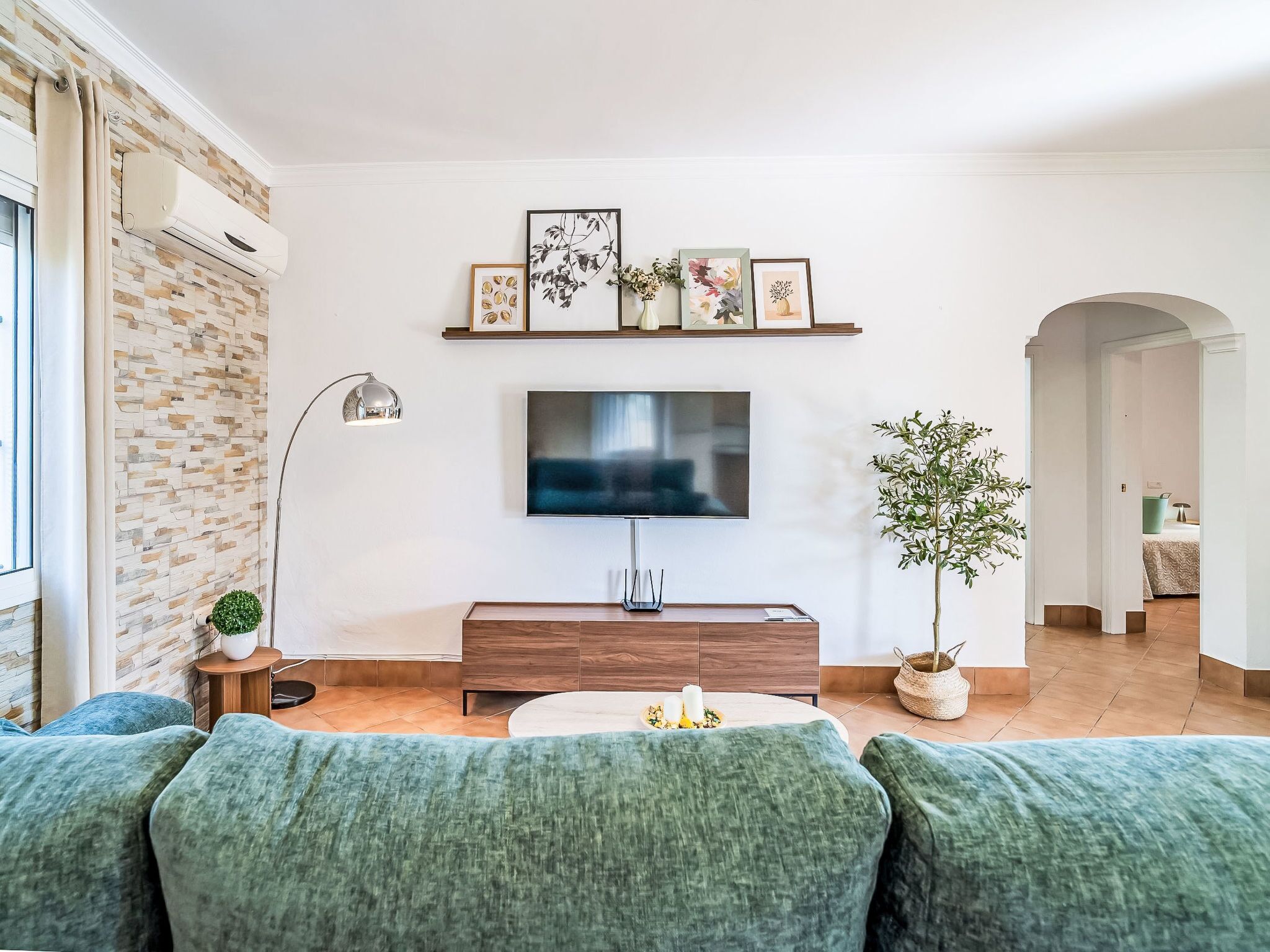 Una sala de estar con televisor de pantalla plana, un sofá, una mesa de centro y una planta en maceta.
