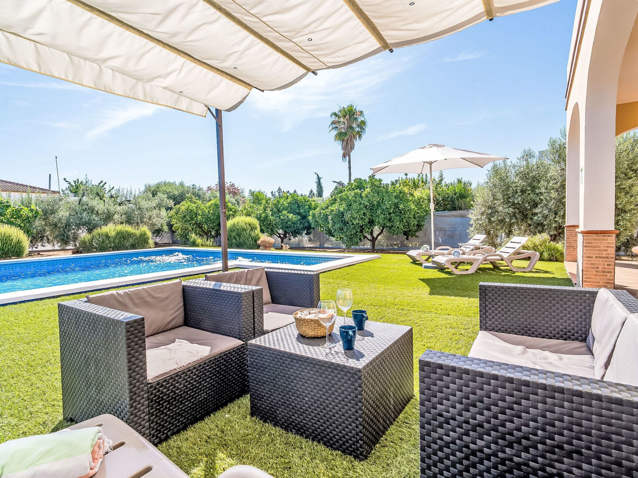 Une terrasse extérieure avec des meubles en osier, une piscine et un ciel dégagé.