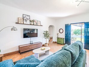 A modern living room with a large flat-screen TV, a blue sofa, a coffee table, and a green cabinet. - Casa Rural Villa Manantial by Interhome (Sevilla/La Puebla de Cazalla)