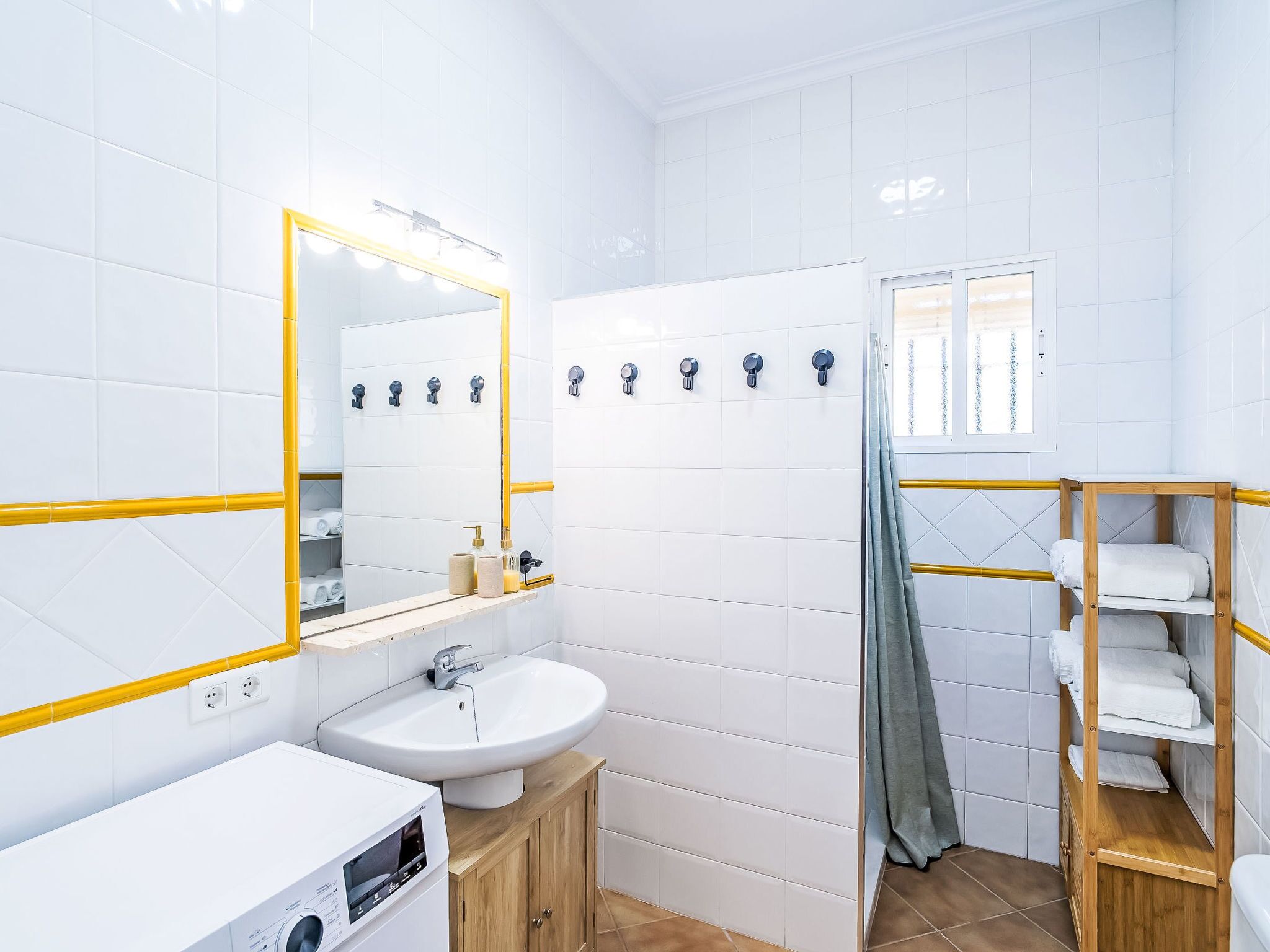 Un baño moderno con azulejos blancos, un espejo grande, un lavamanos y una zona de ducha.