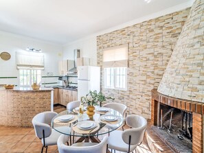 Eine moderne Küche mit einer Steinwand und einem Kamin. Ein Esstisch mit Stühlen und eine Blumenvase sind ebenfalls vorhanden.