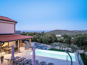 A pool area with lounge chairs and a covered seating area, surrounded by a landscaped garden and a view of distant hills. - Dominika by Interhome (Motovun)