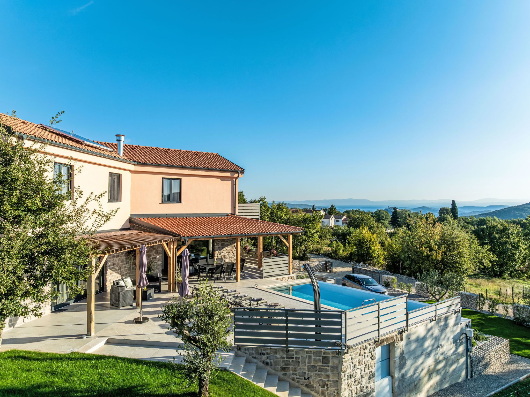 A two-story house with a swimming pool, outdoor seating, and a view of the countryside.