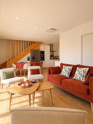 Ein modernes Wohnzimmer mit einer Holztreppe, einem roten Sofa und einem Essbereich mit Tisch und Stühlen.