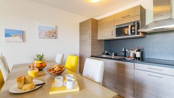 A modern kitchen with stainless steel appliances, a dining area with a table set for breakfast, and two beach-themed wall art pieces.