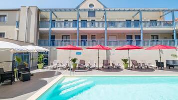 A hotel with a swimming pool, sun loungers, and umbrellas.