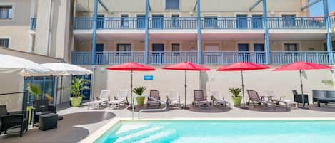 A hotel with a swimming pool, sun loungers, and umbrellas.