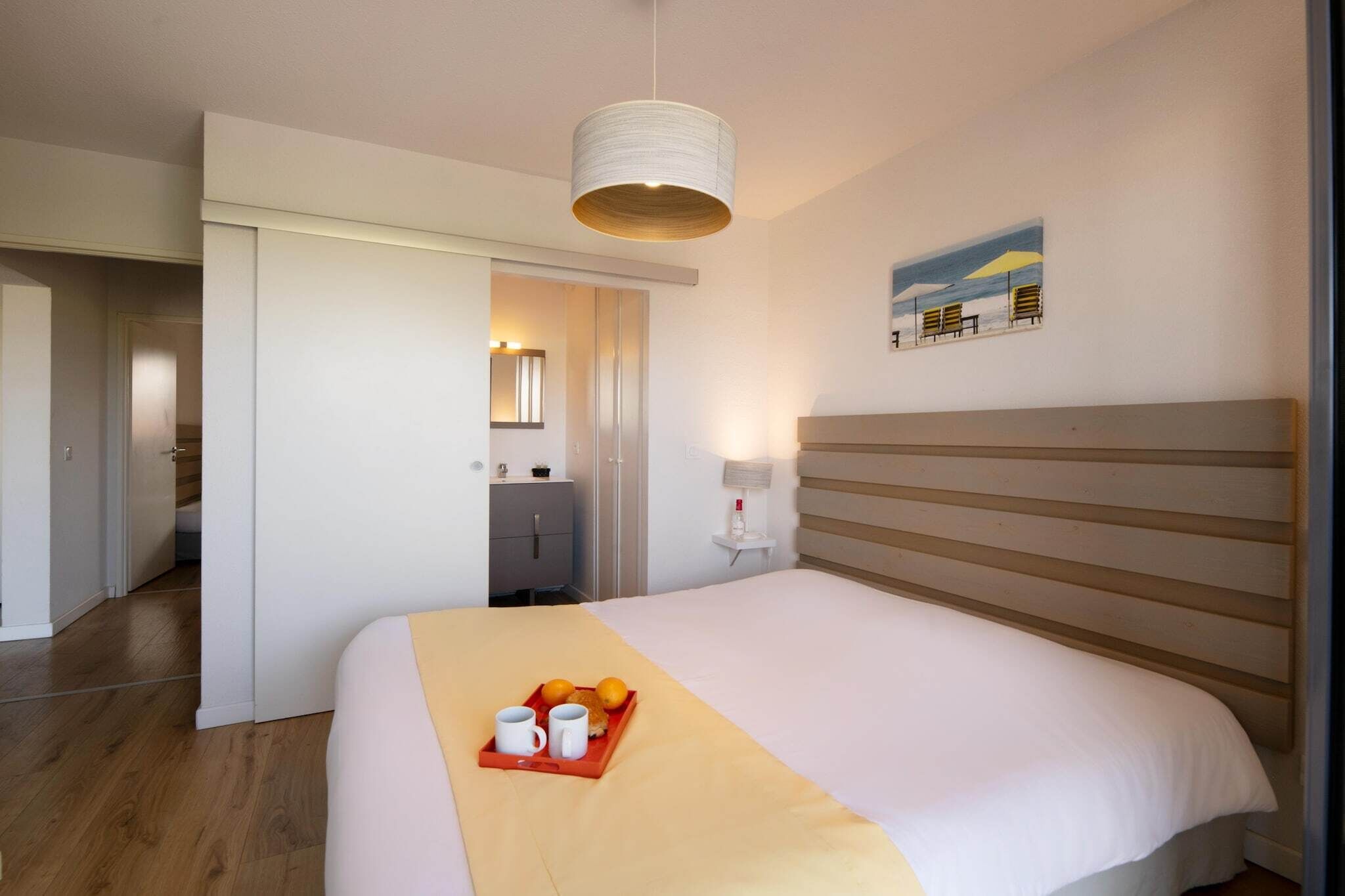 Een hotelkamer met een bed, een nachtkastje met een dienblad met ontbijtartikelen, een hanglamp en een schilderij aan de muur.