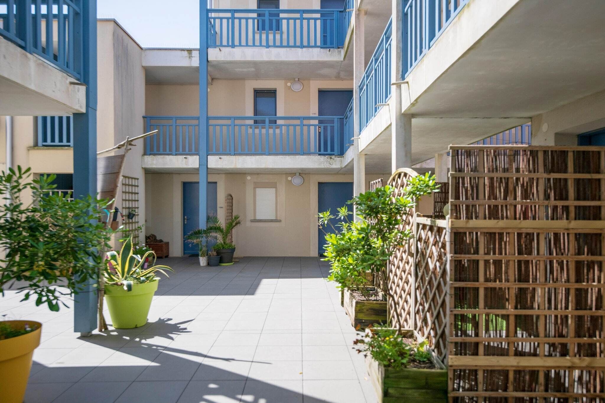 Um pátio com plantas em vasos, um cercado de madeira e um edifício com sacadas.