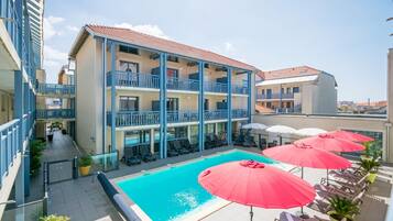 Ein Hotel mit Schwimmbad, mehreren Balkonen und Sitzgelegenheiten im Freien mit Sonnenschirmen.