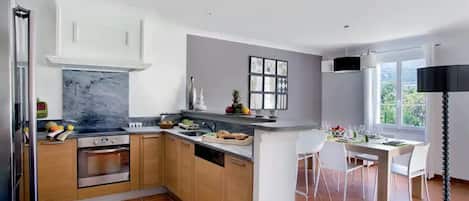 Una cocina moderna con armarios de madera, salpicadero de mármol y comedor con mesa y sillas blancas.