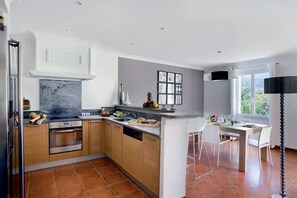 Eine moderne Küche mit Holzschränken, einer Marmor-Spritzschutzleiste und einem Essbereich mit einem weißen Tisch und Stühlen.