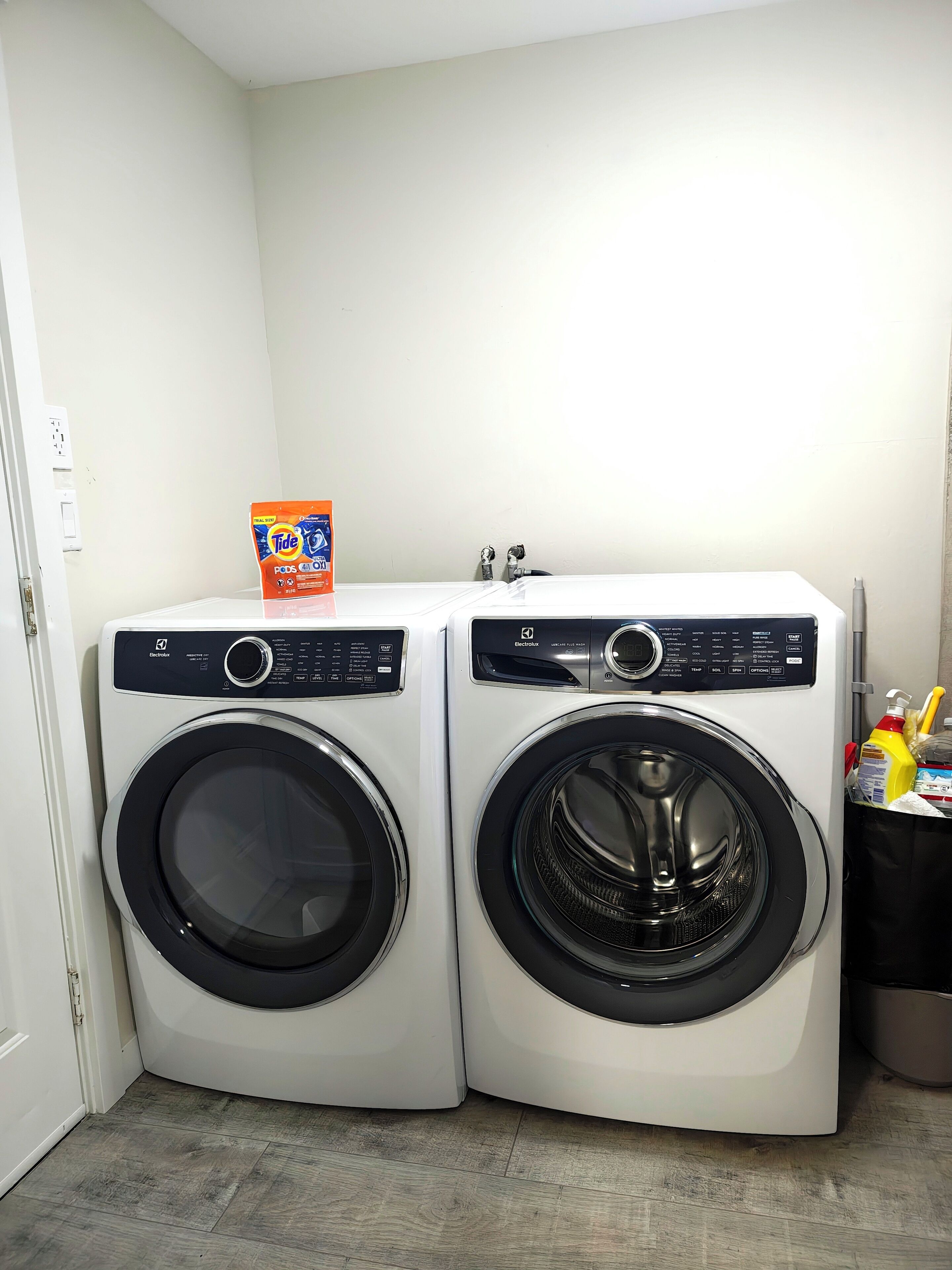 A laundry area with two front-loading washing machines and a bag of Tide detergent on the left.
