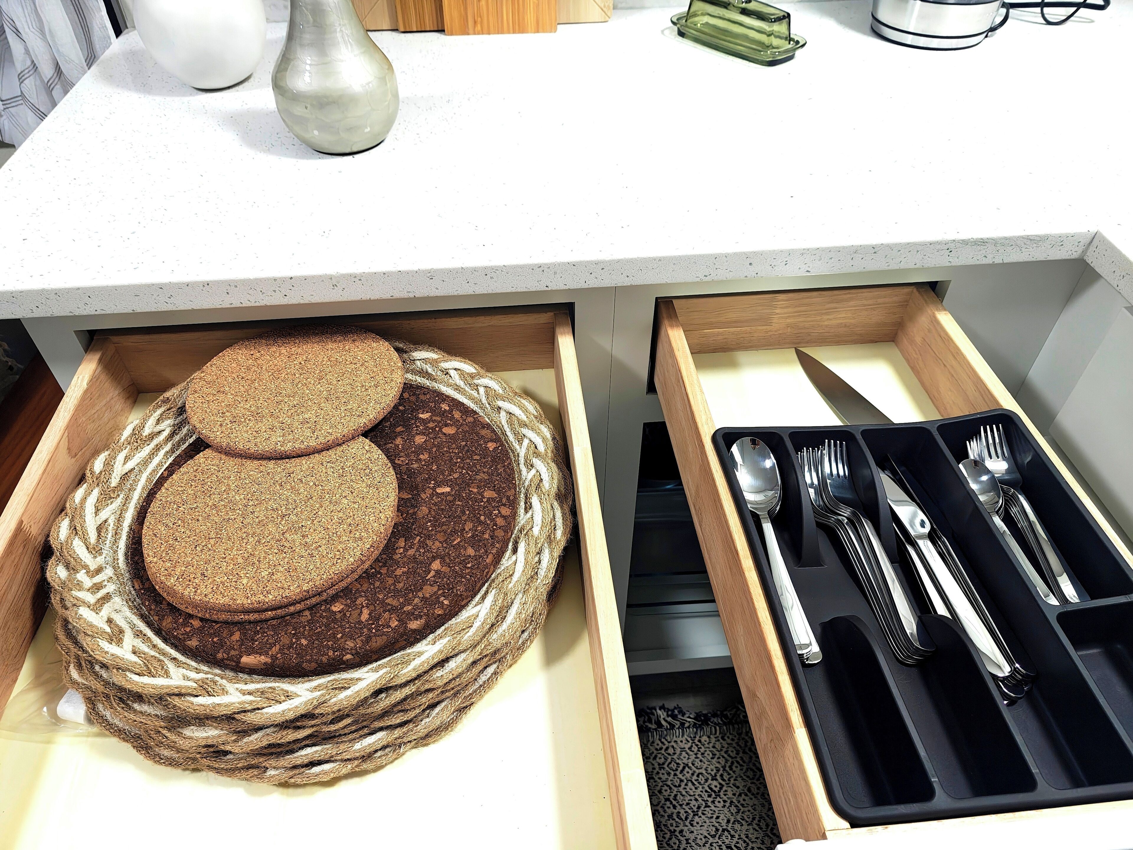 Un cajón de cocina con una cesta tejida que contiene pan y un organizador de utensilios con cubiertos.