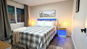 Ein Schlafzimmer mit einem Bett, Nachttischlampen, einem Nachttisch, einem Fenster mit Vorhängen, einem Bild an der Wand und einem gemusterten Teppich.