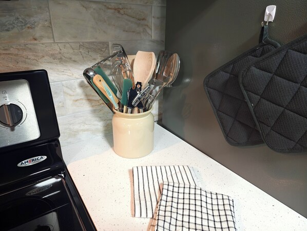 A kitchen counter with a stove, a utensil holder, and a striped cloth.