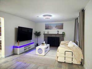 A modern living room with a flat-screen TV, a fireplace, a sofa, and a decorative plant.