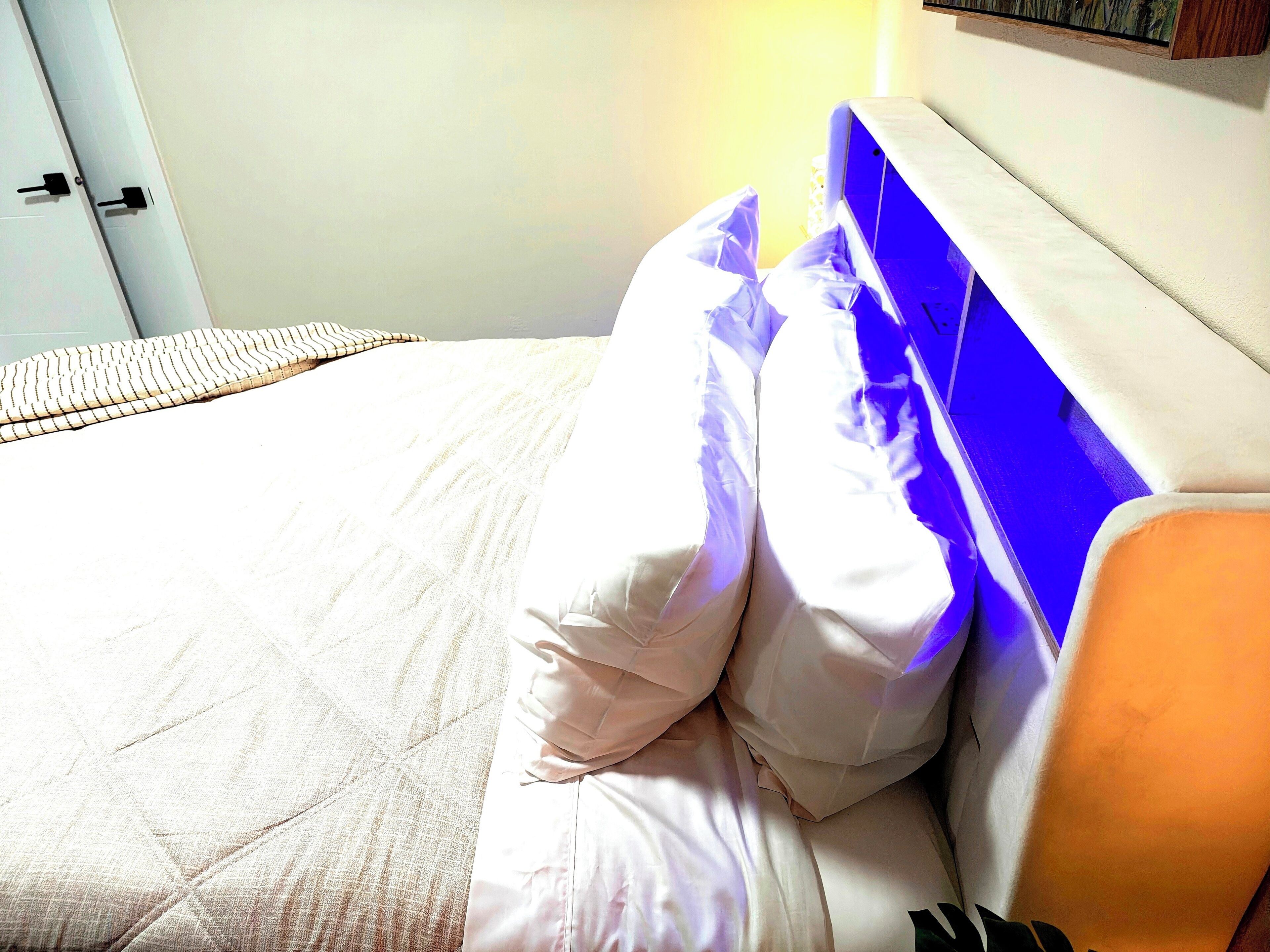 A bed with white bedding and a blue headboard, a bedside table, and a wall-mounted shelf.