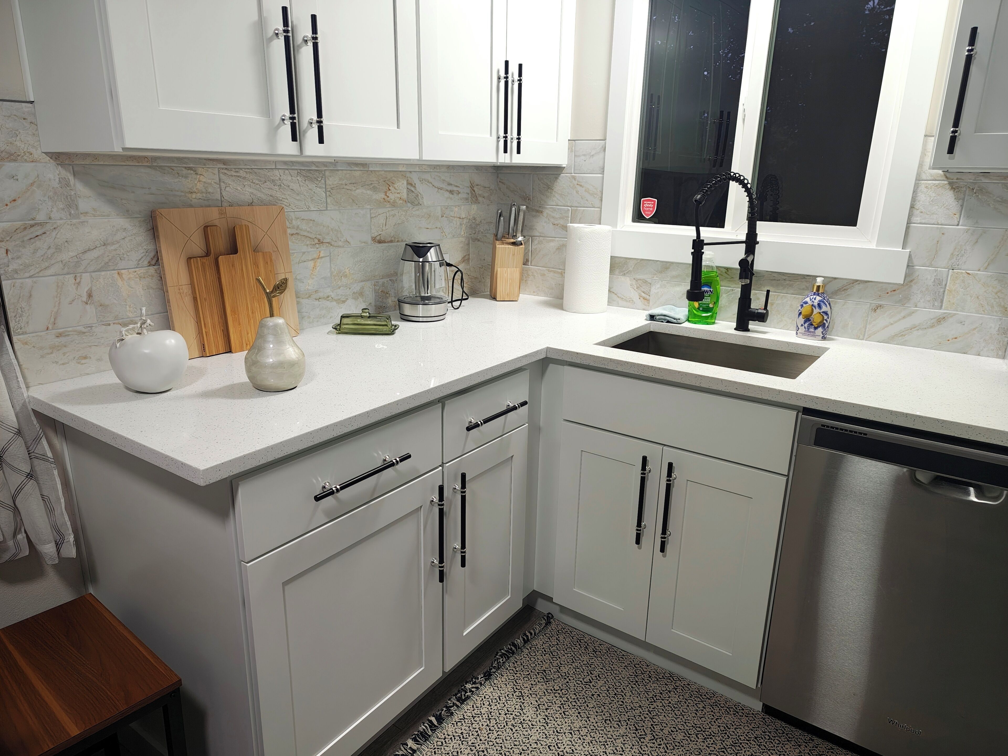 Una cocina moderna con armarios blancos, lavavajillas de acero inoxidable y una ventana con vistas.