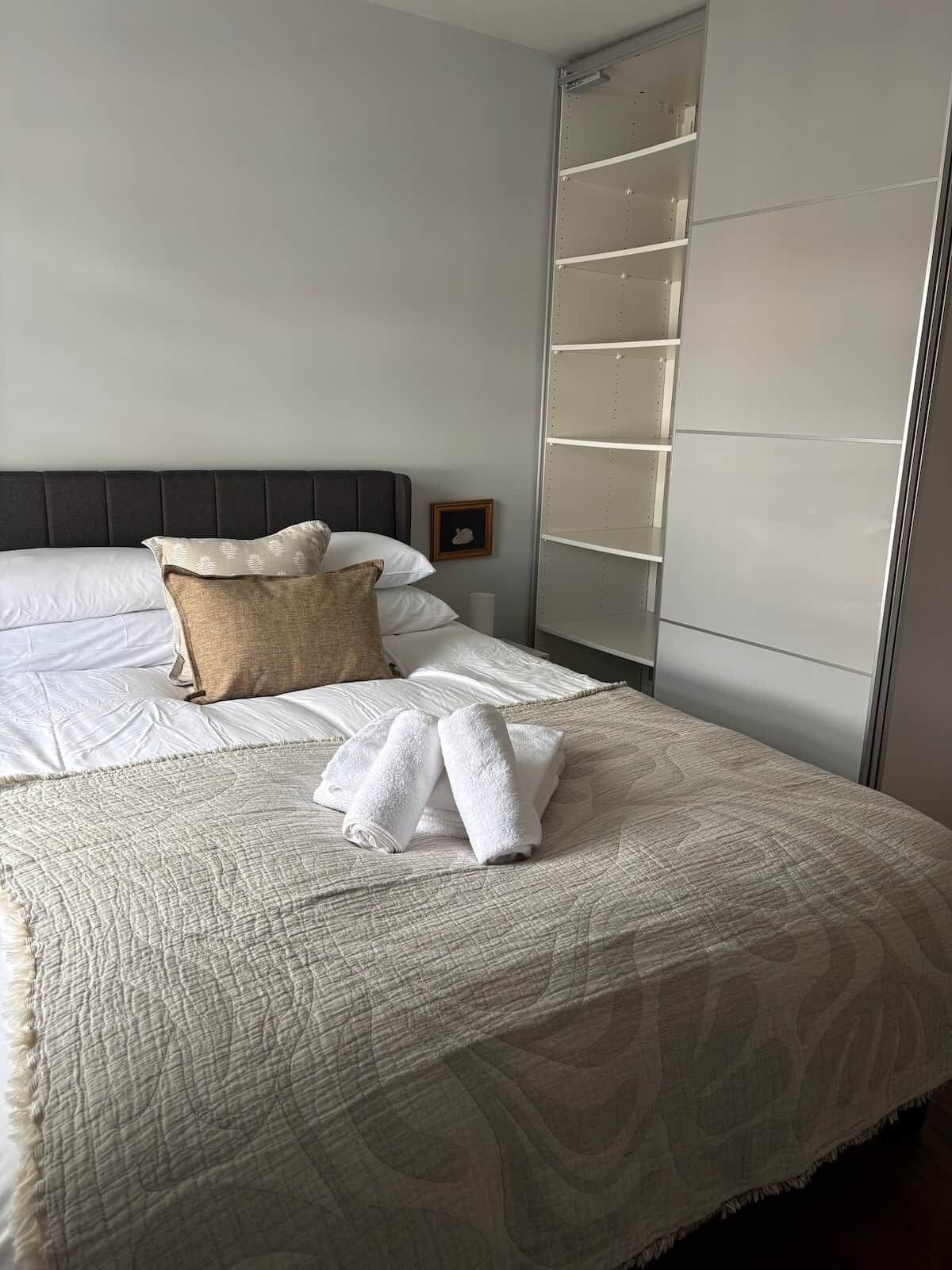 A neatly made bed with a quilted cover, a pillow, and rolled towels.