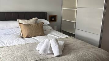 A neatly made bed with a quilted cover, a pillow, and rolled towels.