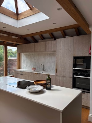 A modern kitchen with a skylight, wooden beams, and a built-in oven.