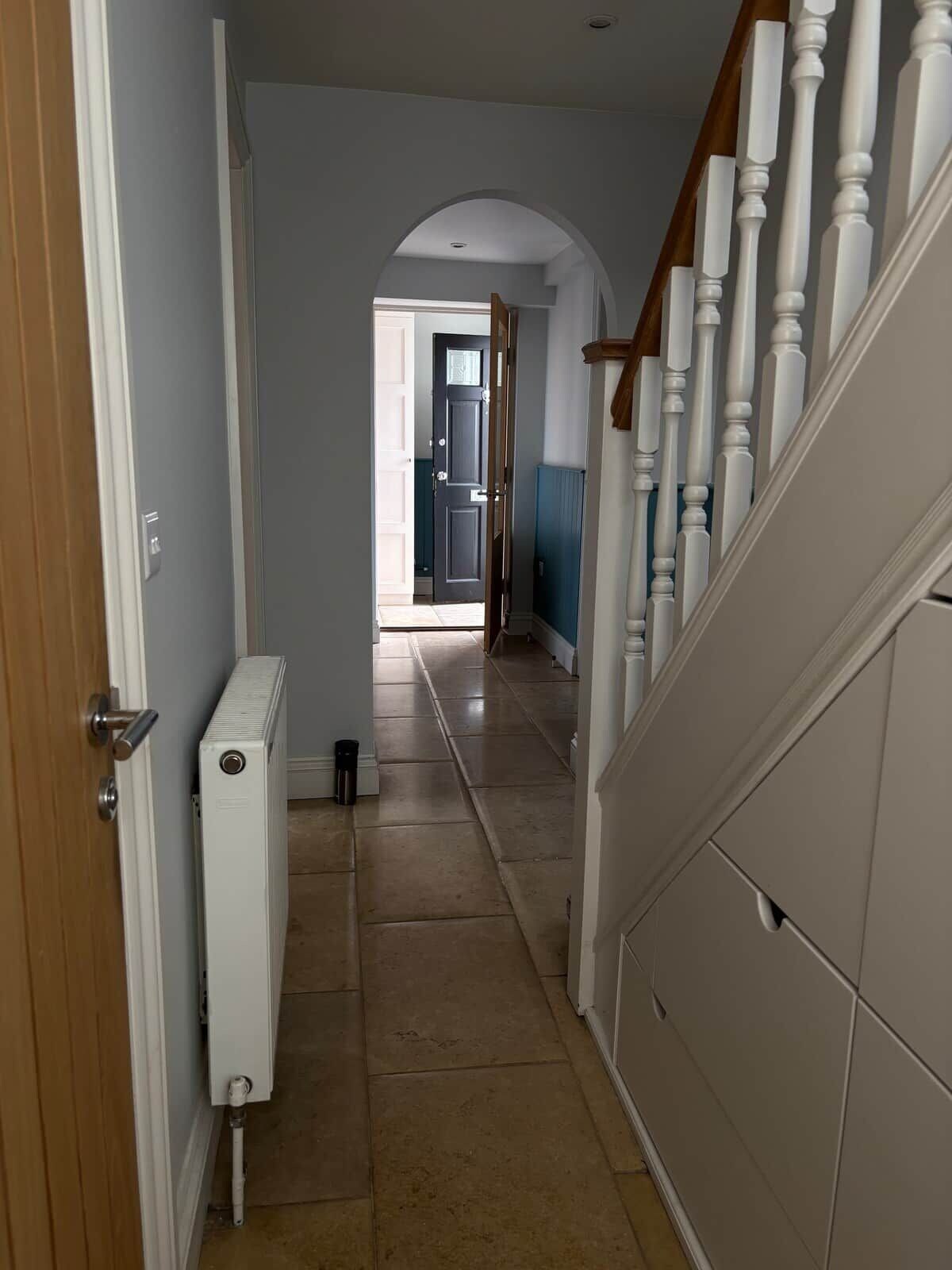 A hallway with a radiator, a wooden door, and a staircase with white balusters.