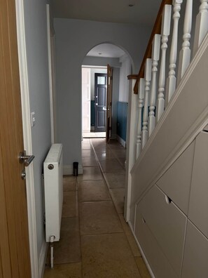 A hallway with a radiator, a wooden door, and a staircase with white balusters.