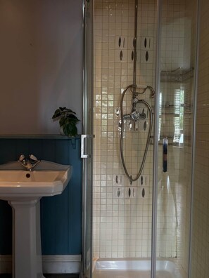 A bathroom with a glass-enclosed shower, a pedestal sink, and a tiled wall.