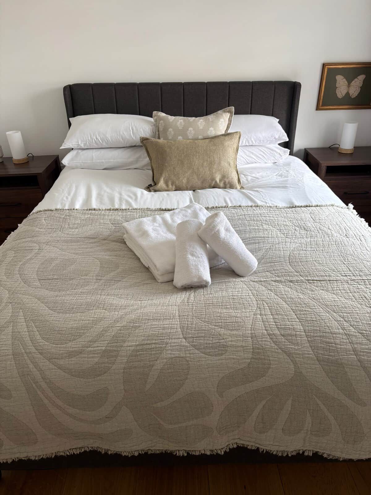 A neatly made bed with a quilted cover, two pillows, and a set of folded towels on the bed.
