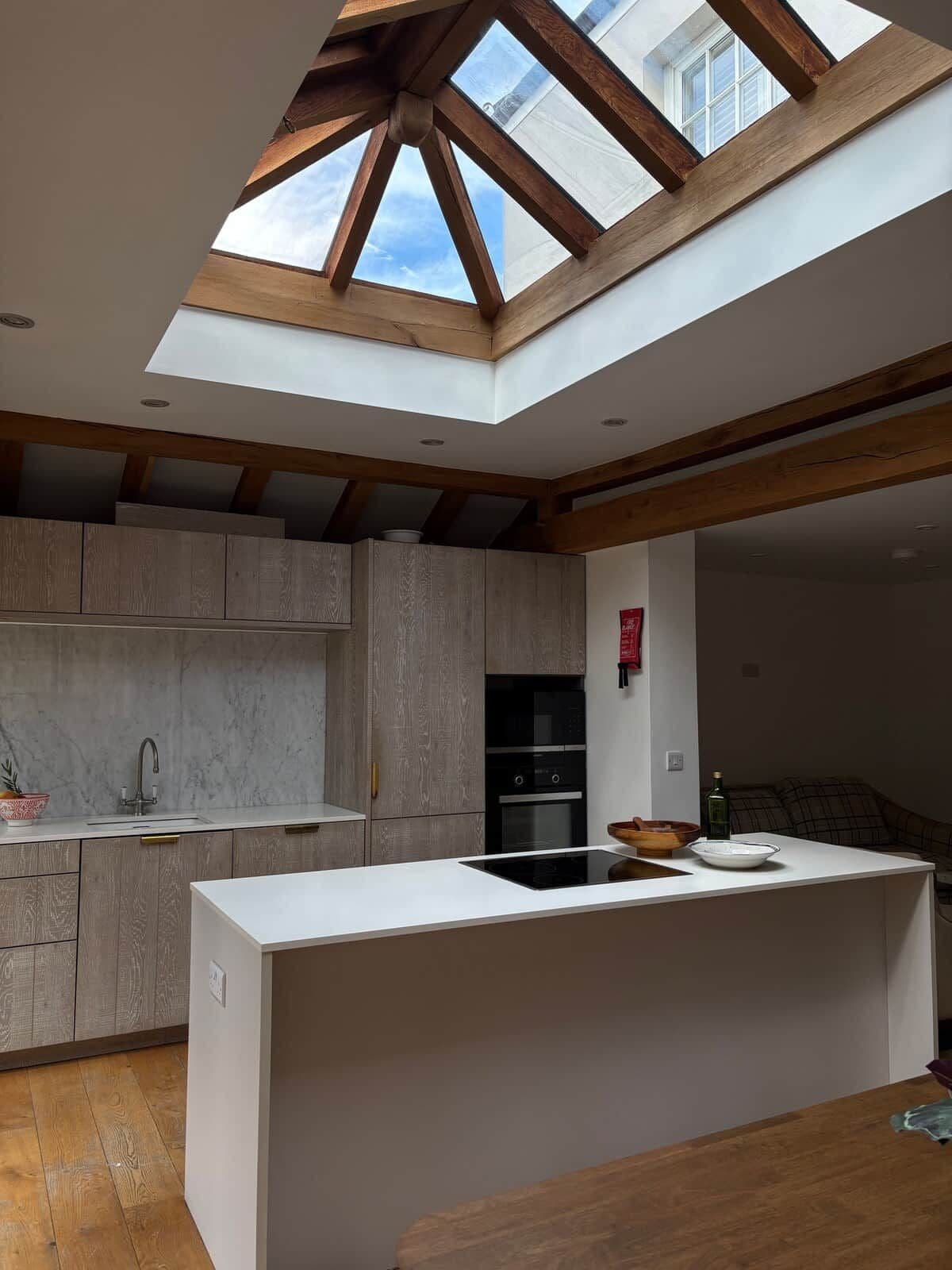 A modern kitchen with a skylight, wooden beams, and a central island.