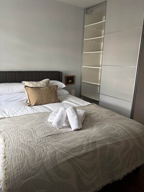 A neatly made bed with a patterned bedspread, a pillow, and rolled towels.