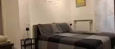 A bedroom with a bed, a nightstand, a lamp, and a wall with a poster.