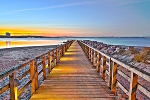 A wooden pier leading to a beach with a calm sea and a sunset in the background. - 4 Port Times - NEVER.6 Venus (Timmendorfer Strand)