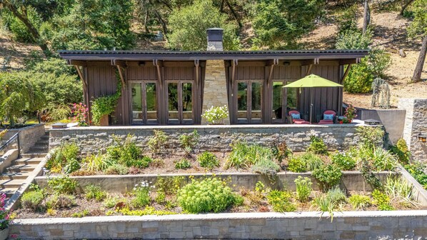 A cabin with a stone foundation, wooden exterior, and a covered patio area with chairs and a table.