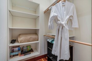 A hotel room with a white robe hanging on a wooden rack, a beige towel on a shelf, and a collection of board games on a lower shelf.
