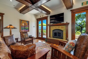 A living room with a fireplace, a television, and a large window with a view of trees.