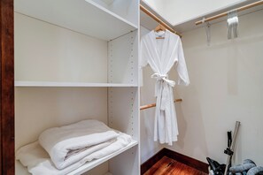 A white robe hanging on a wooden hanger in a closet with shelves and a wooden floor.