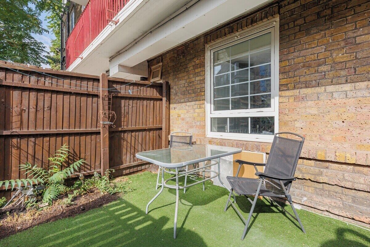 Eine Terrasse mit Tisch und Stühlen, ein Holzzaun und eine Ziegelwand mit Fenster.
